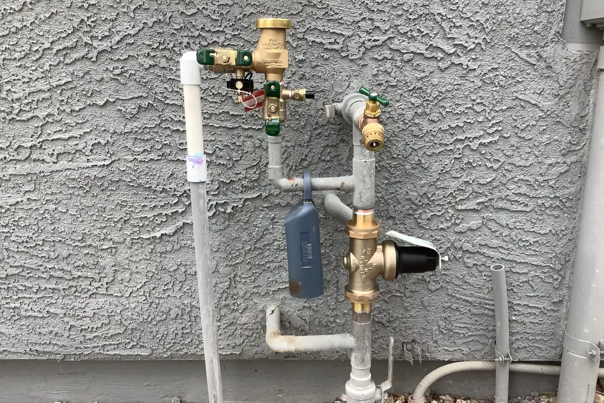 A pressure vacuum breaker, pressure reducing valve and hose bib on a home's water line against a stucco wall