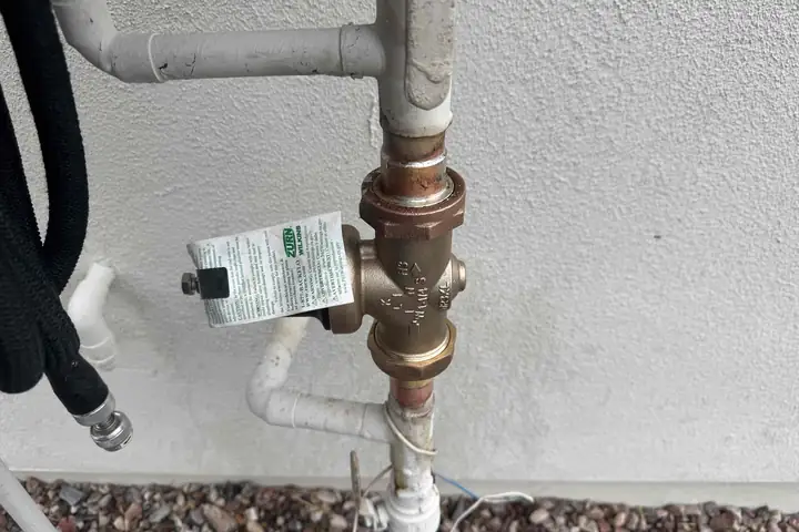 A newly installed pressure reducing valve, product tag still attached, on a home's water line beside a stucco wall