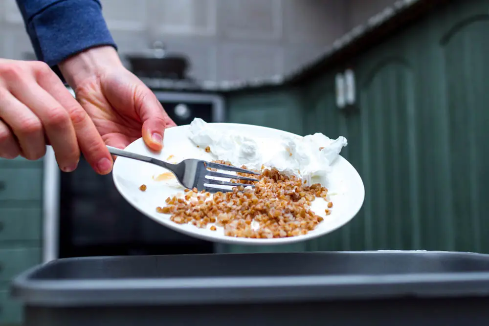 a person scraping food waste off a plate and into a trash bin