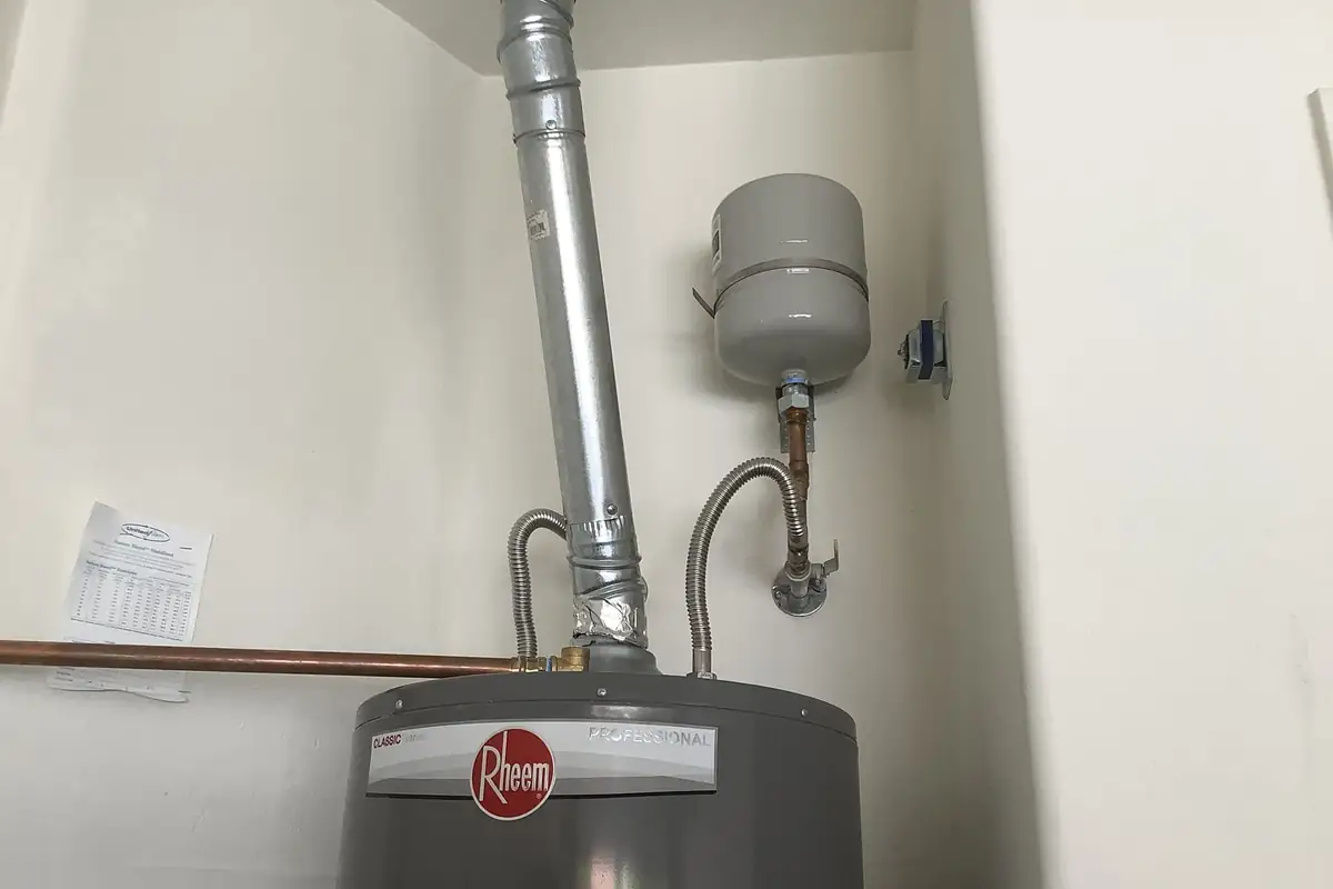 A tank water heater with a thermal expansion tank mounted on the wall above its cold-water line