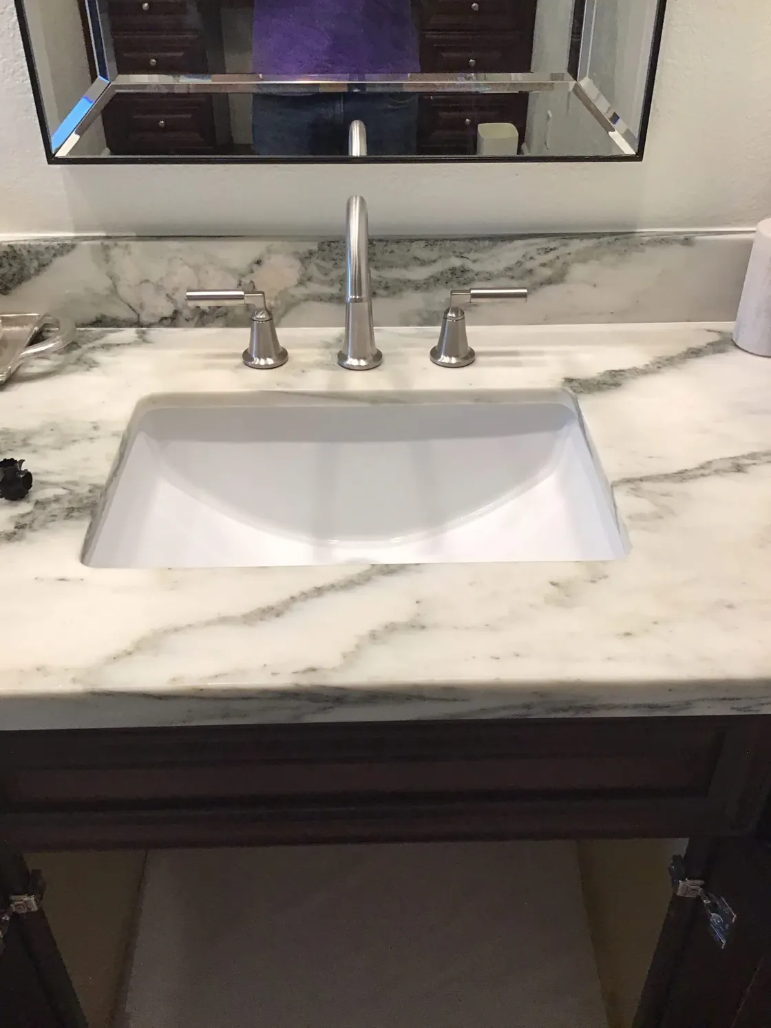 A chrome bathroom faucet above a white sink and marble counter