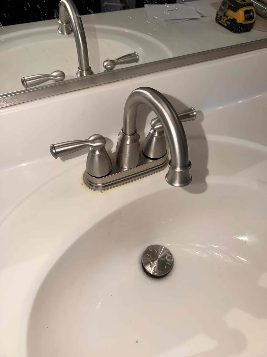 A brushed nickel two-handle faucet on a white bathroom sink