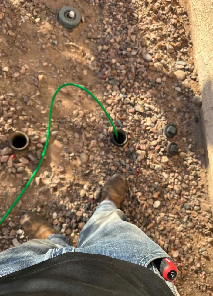 A drain cable entering an outdoor cleanout in a gravel yard