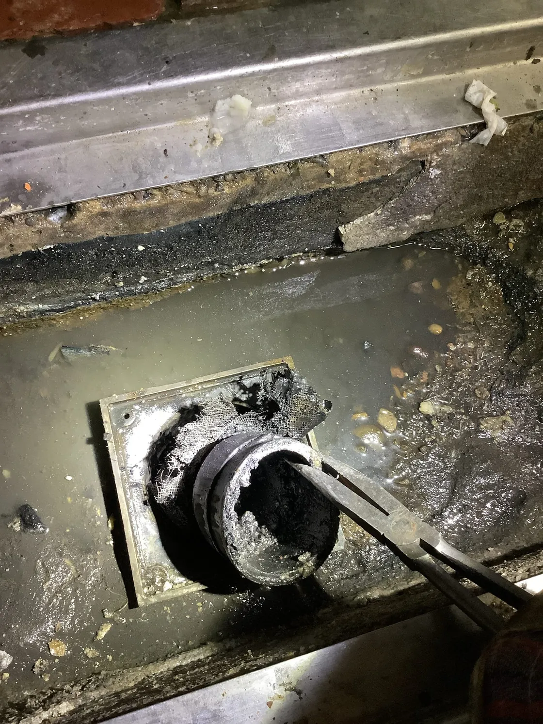 A tool removing a broken piece from a commercial floor drain
