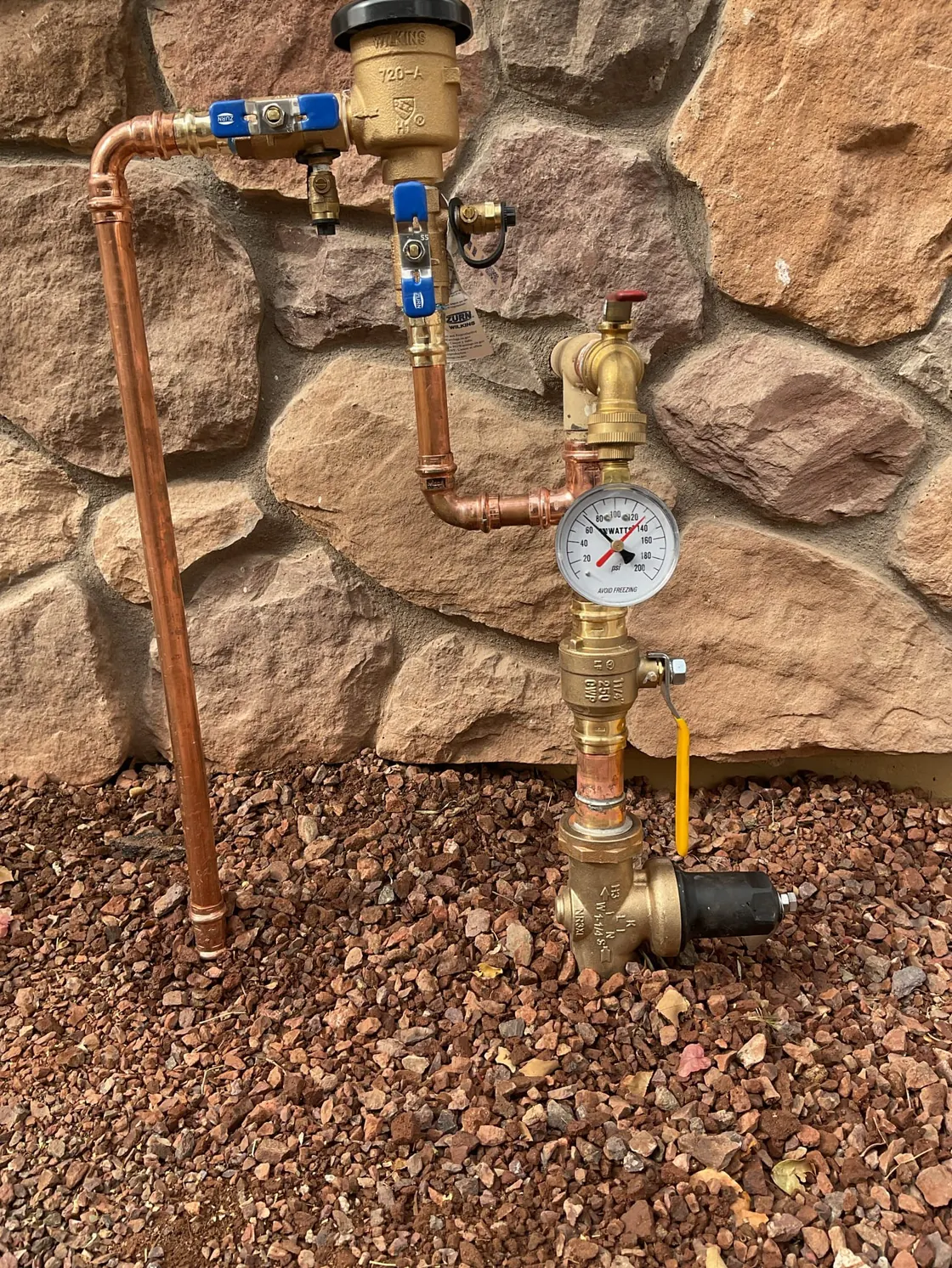 New copper supply piping with a pressure gauge and valves against a stone wall