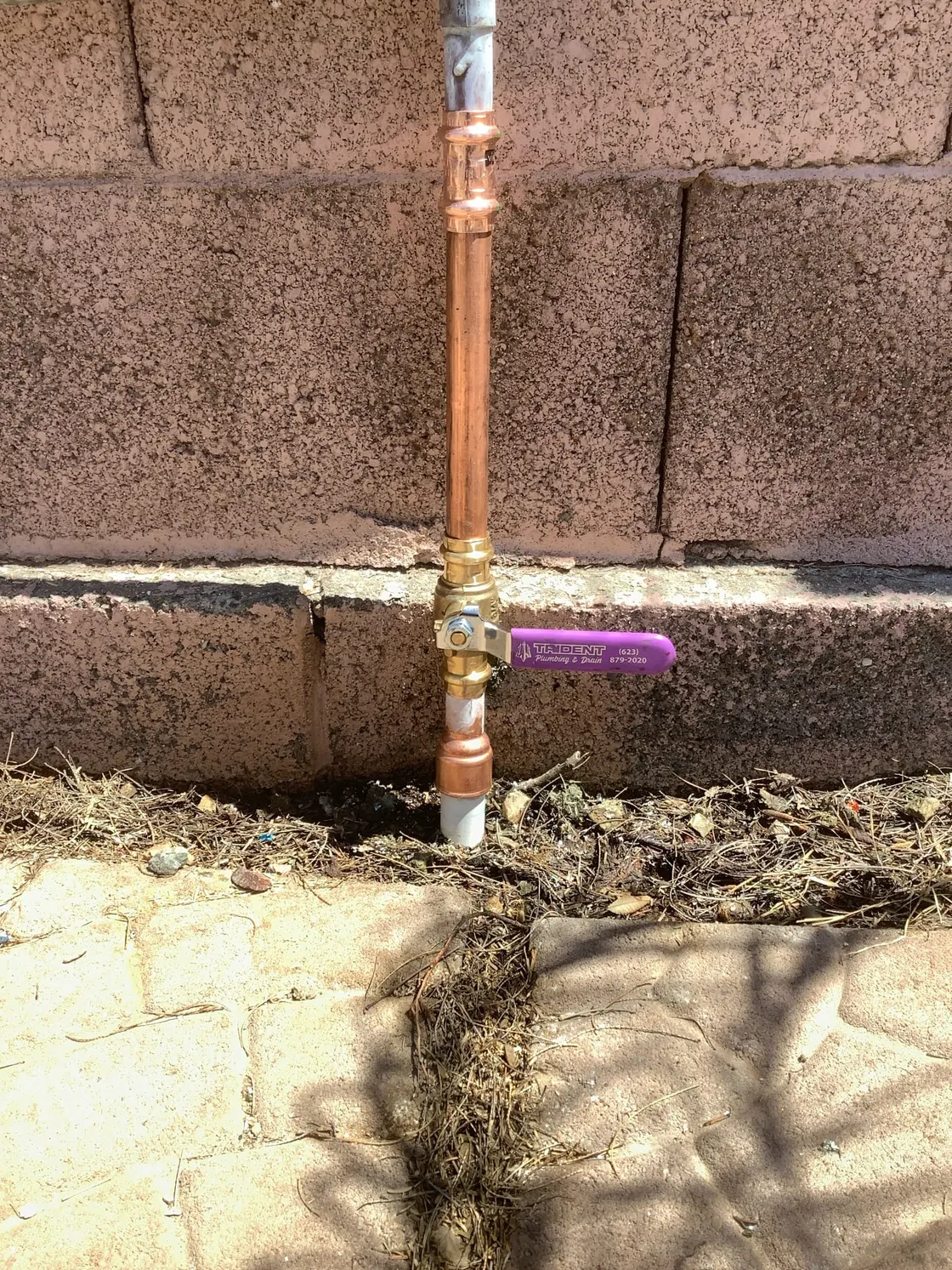 A new copper supply pipe and shutoff valve rising from the ground beside a block wall