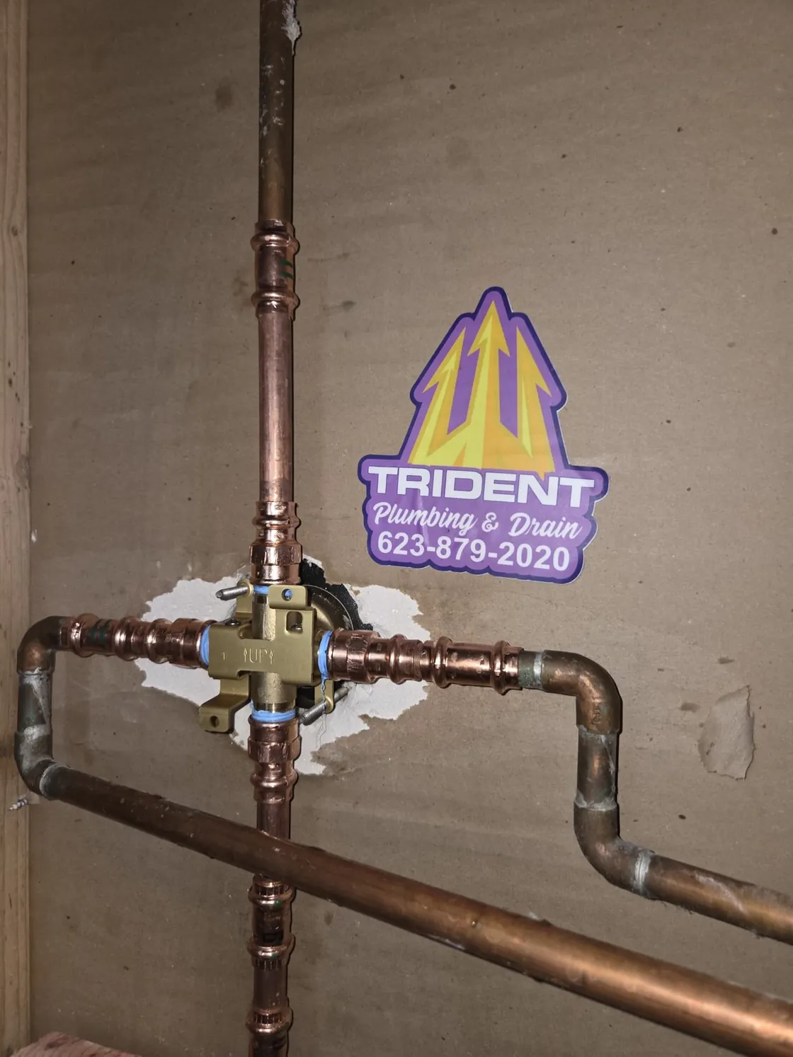 New copper water piping and a valve body on a wall with a Trident sticker beside it