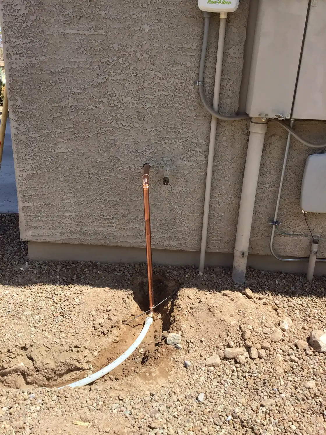 A new copper water line rising from a trench beside a stucco wall