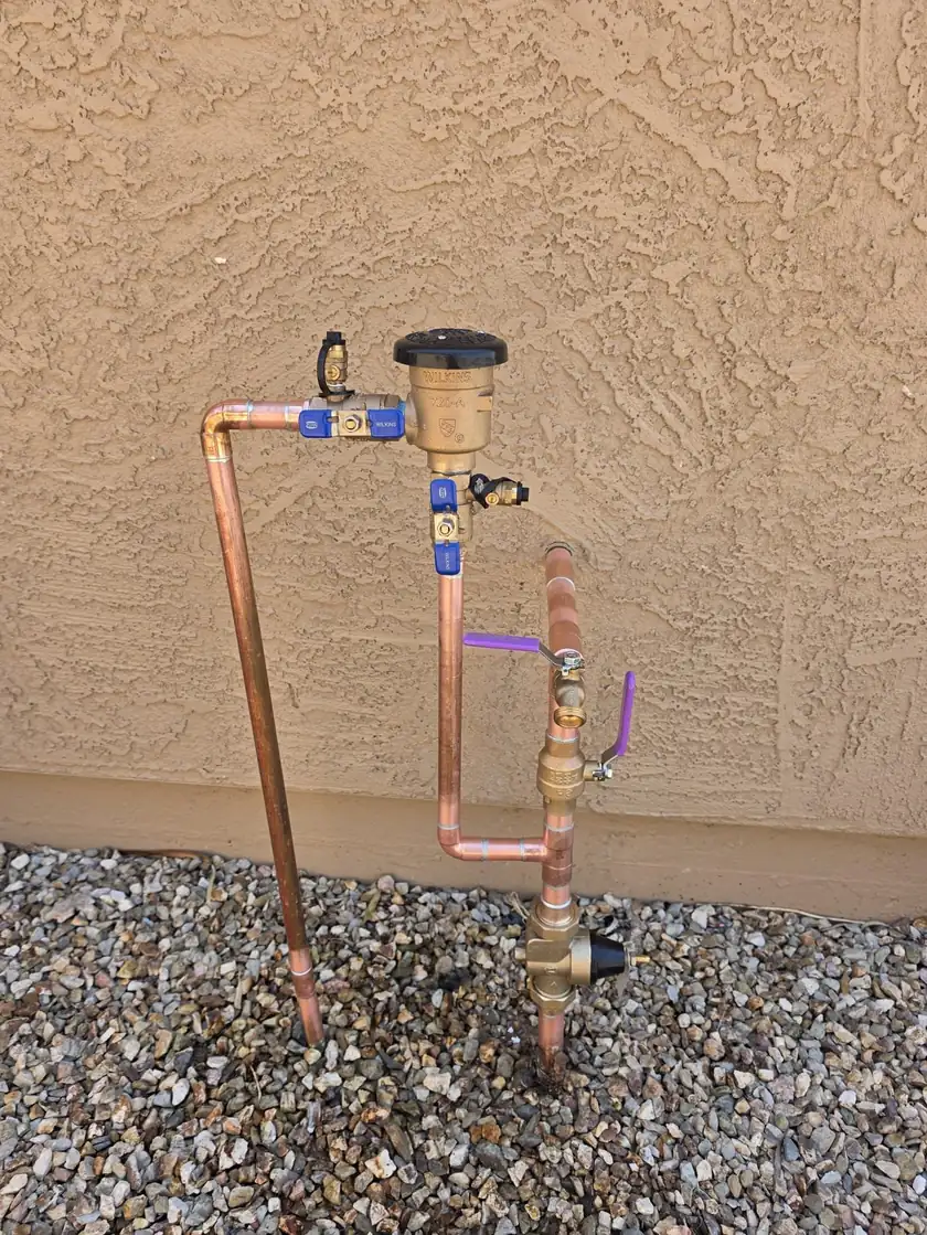 A copper water supply assembly with valves and a regulator mounted on a stucco wall