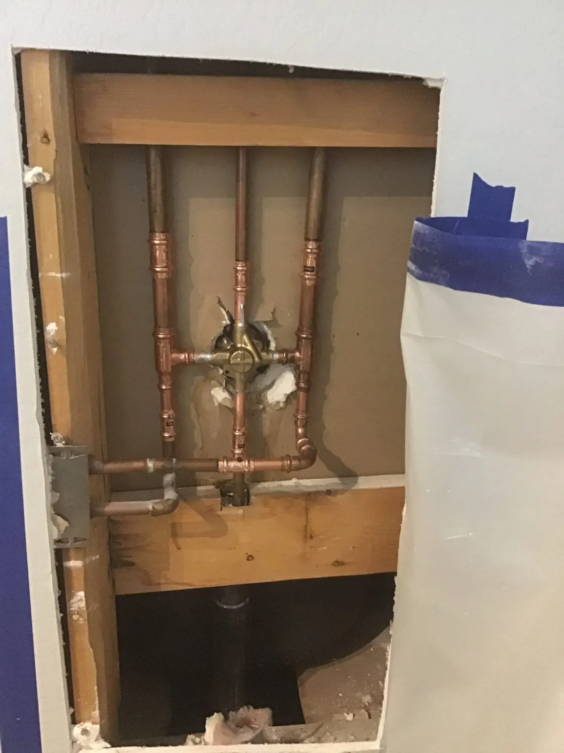 Copper supply lines and a shower valve visible through a large opening cut in a wall