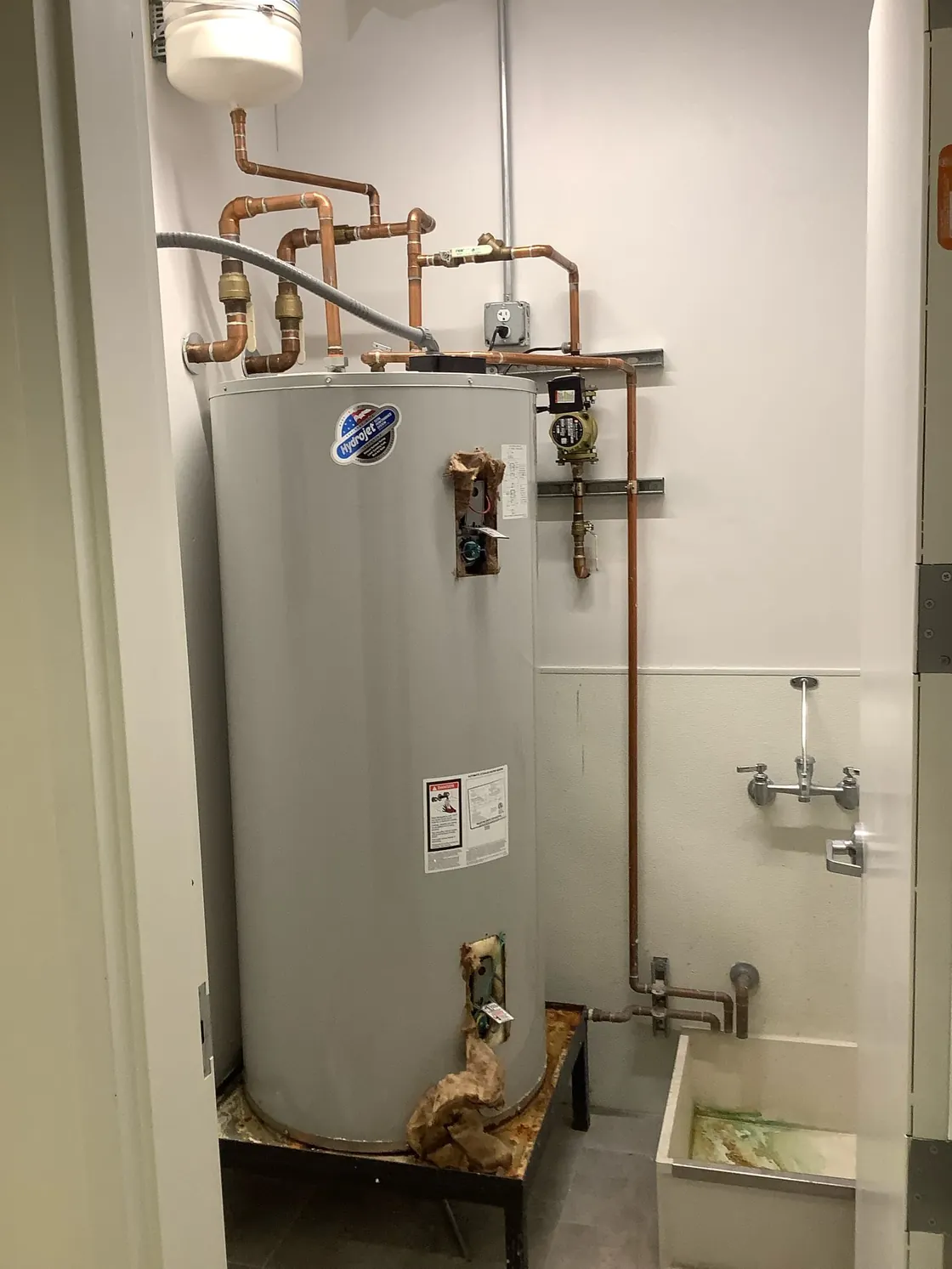 An older tank water heater with corrosion around its base and drain pan