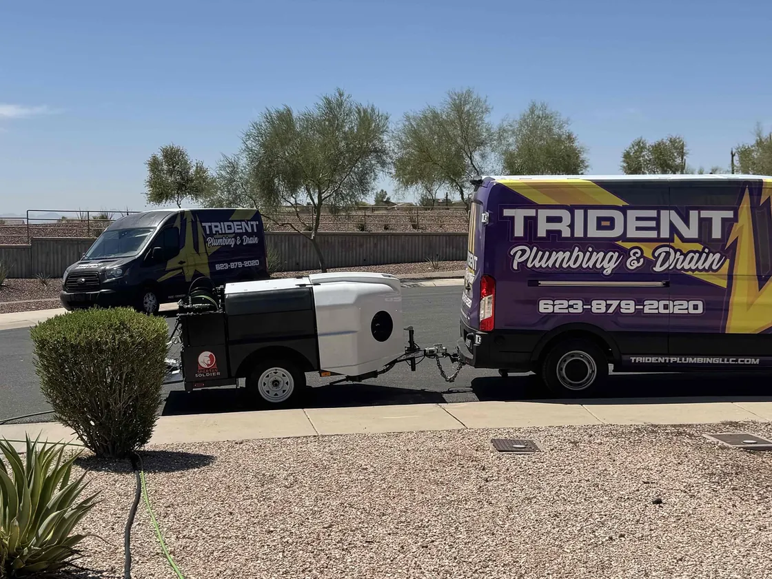 Two Trident vans and a trailer-mounted drain jetter parked at a curb