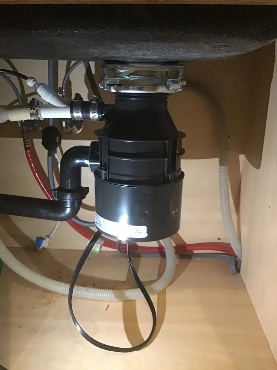 A garbage disposal under a kitchen sink with its drain and supply connections