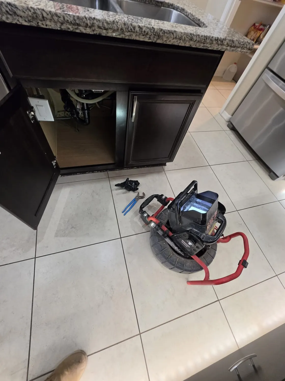 Drain inspection equipment set up beside an open sink cabinet