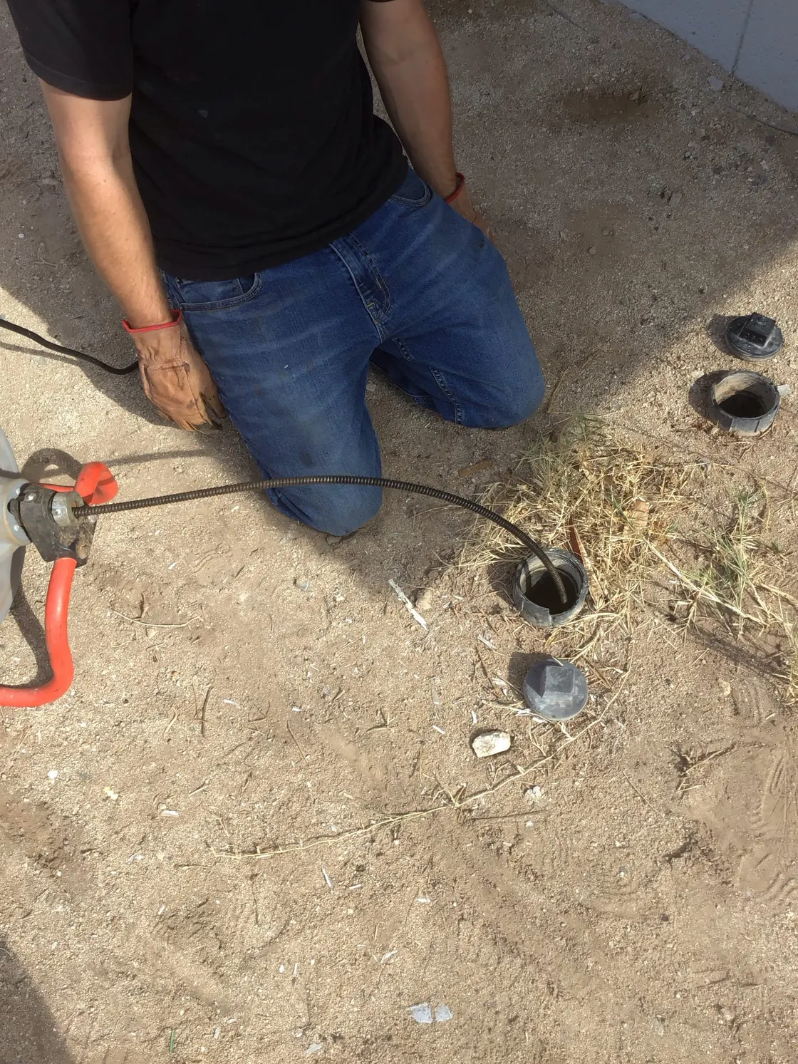 A technician feeding a drain cable into an outdoor sewer cleanout