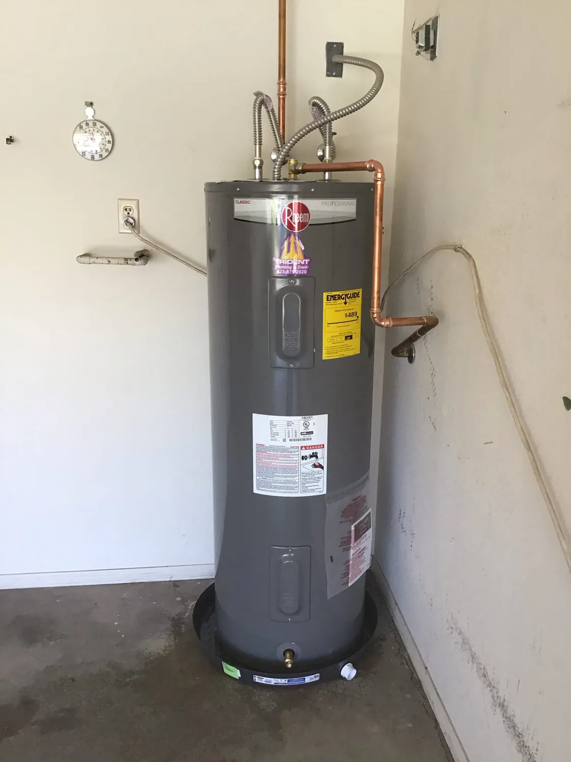An electric tank water heater on a drain pan in a laundry space