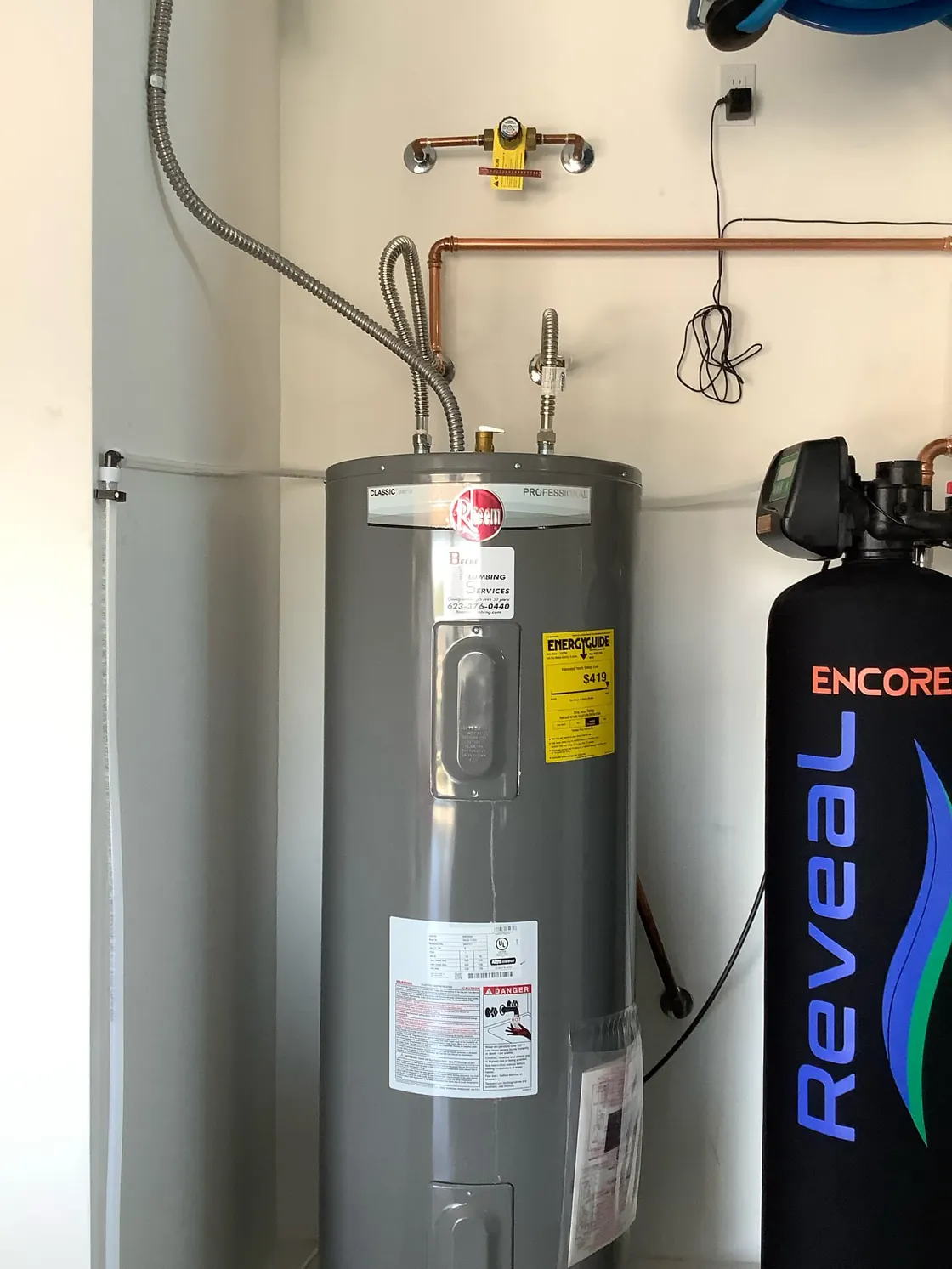 An electric tank water heater beside an Encore Reveal treatment tank in a laundry area