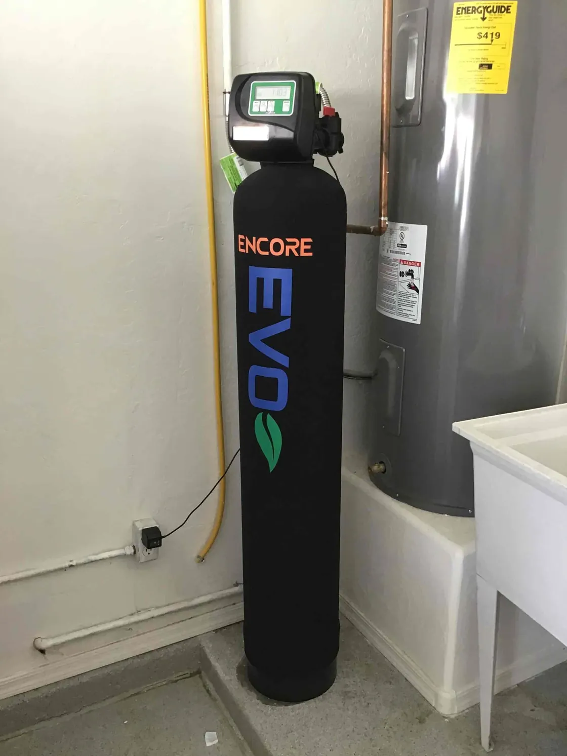 An Encore EVO water treatment tank beside a water heater in a laundry area