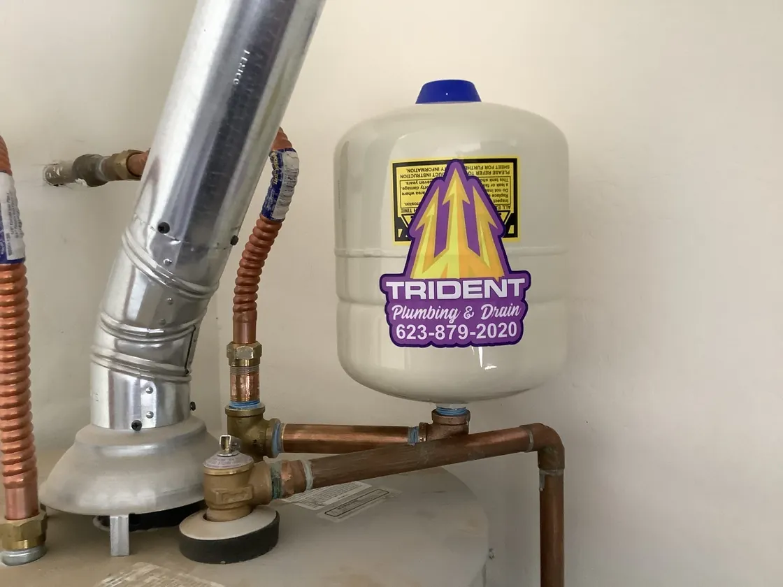 An expansion tank with a Trident label above a water heater's vent and connections