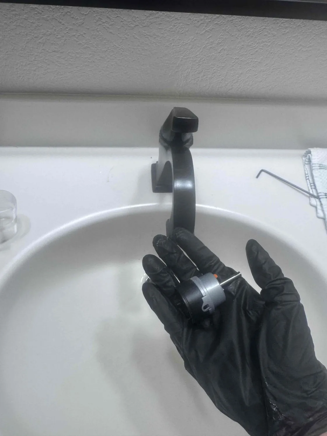 A technician holding a faucet cartridge above a bathroom sink