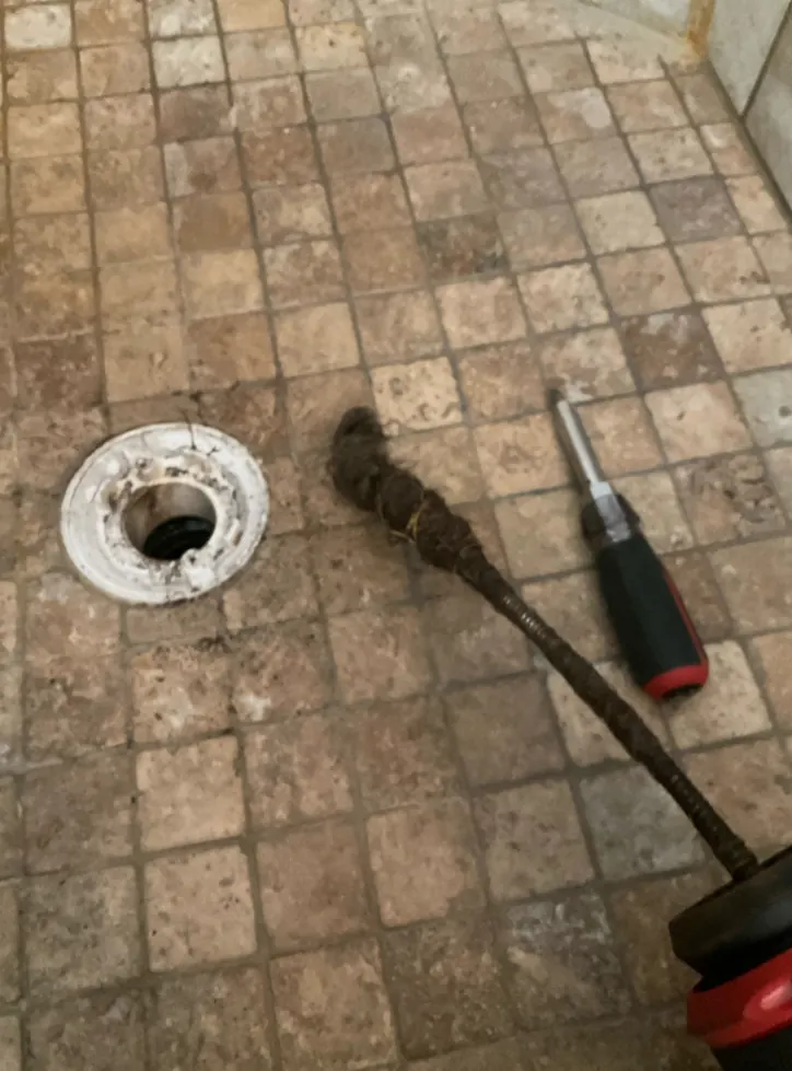 A drain cable and tool beside an open floor drain in a tiled shower