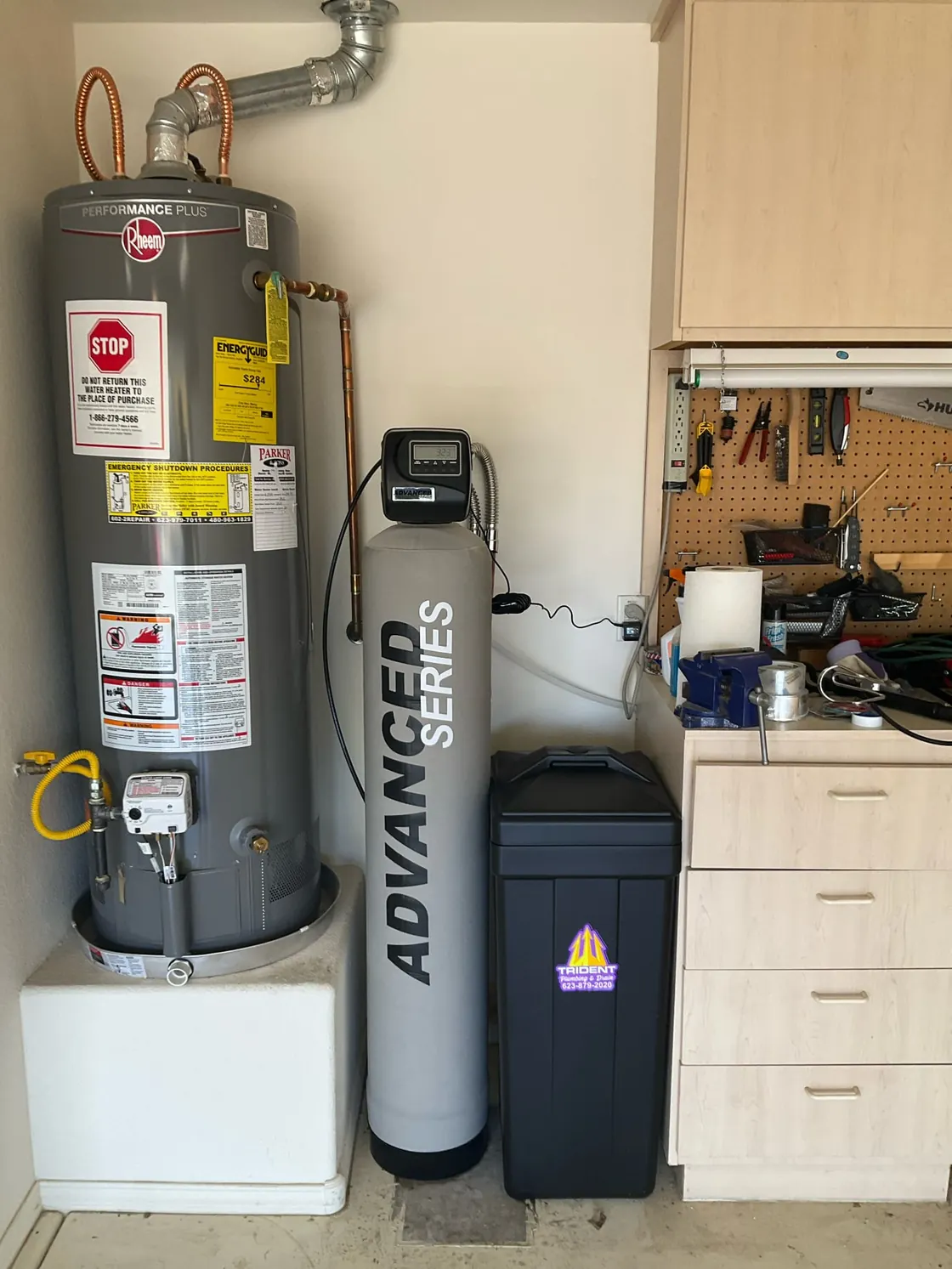 A gas tank water heater on a platform next to water treatment equipment in a garage