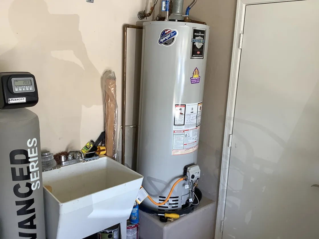A gas tank water heater installed on a platform in a garage beside a utility sink
