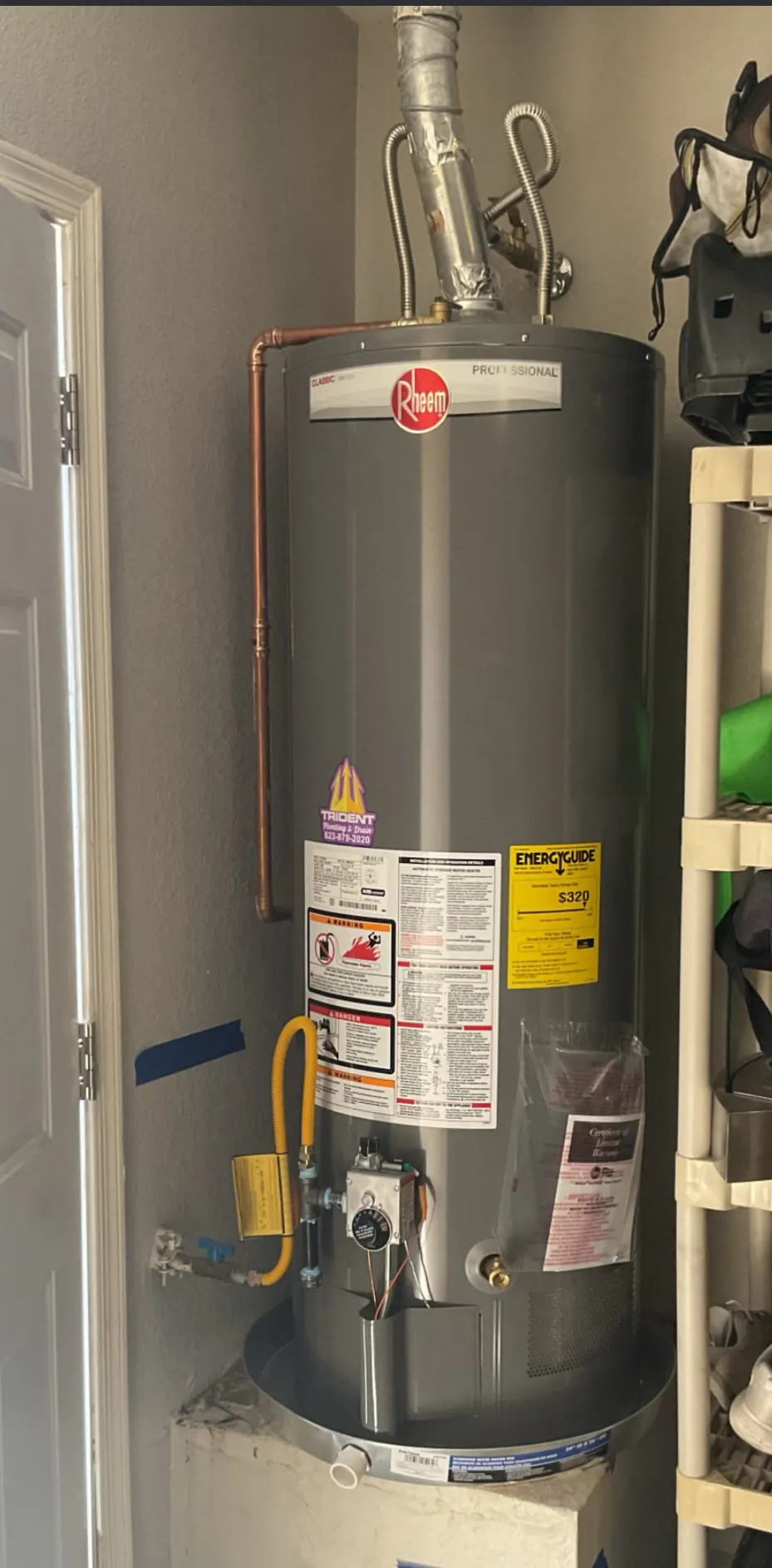 A gas tank water heater against a garage wall with copper and gas connections