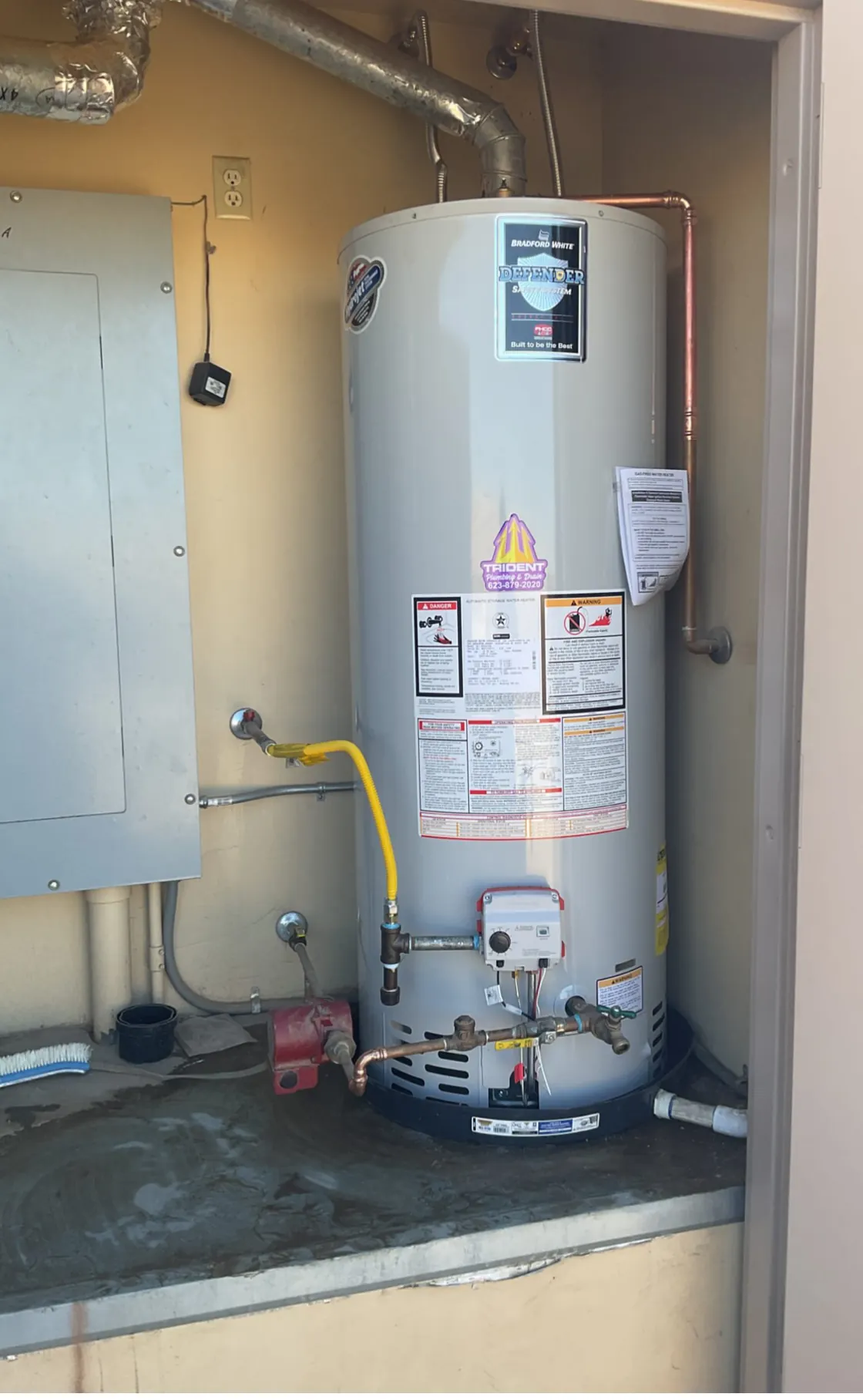 A gas tank water heater in a utility room beside an electrical panel