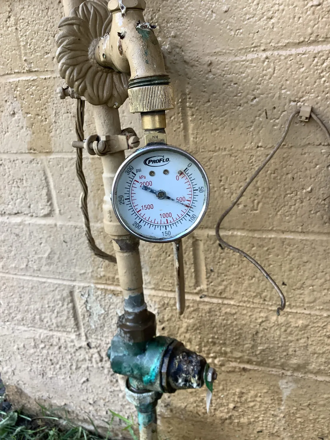 A water pressure gauge attached to an older outdoor spigot on a block wall