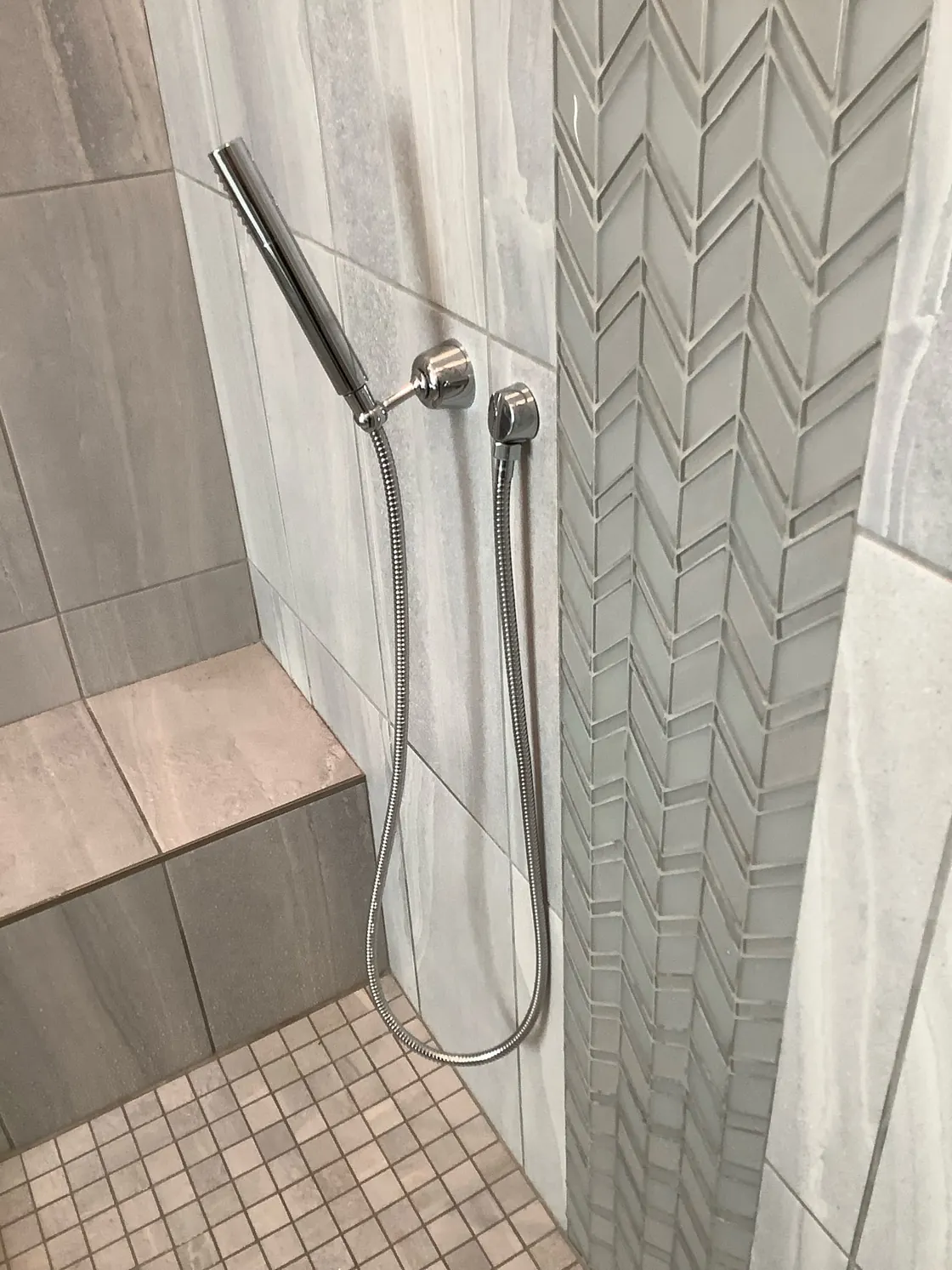A handheld shower spray mounted on a tiled shower wall