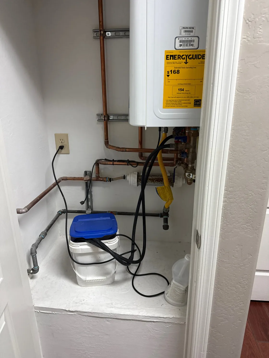A tankless water heater connected to a bucket and service hoses for maintenance