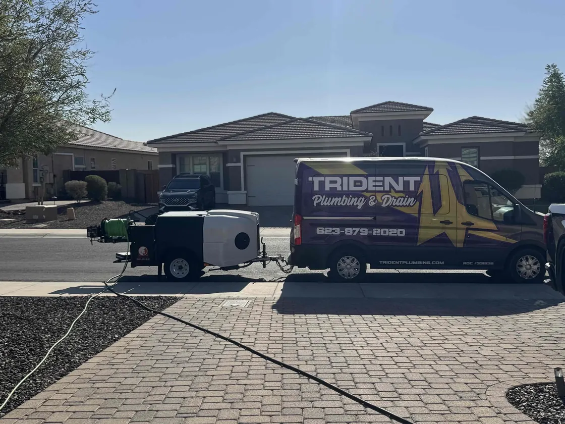 A Trident van and jetting trailer parked in front of a home with hose run across the driveway