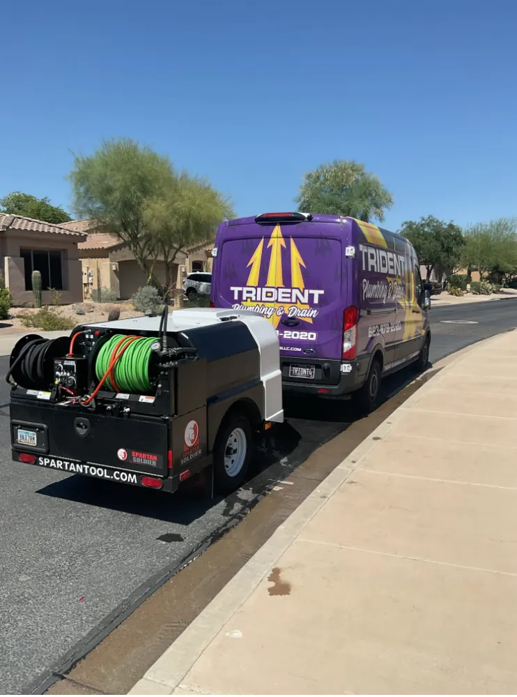 A trailer-mounted drain jetter hitched behind a Trident van on a residential street