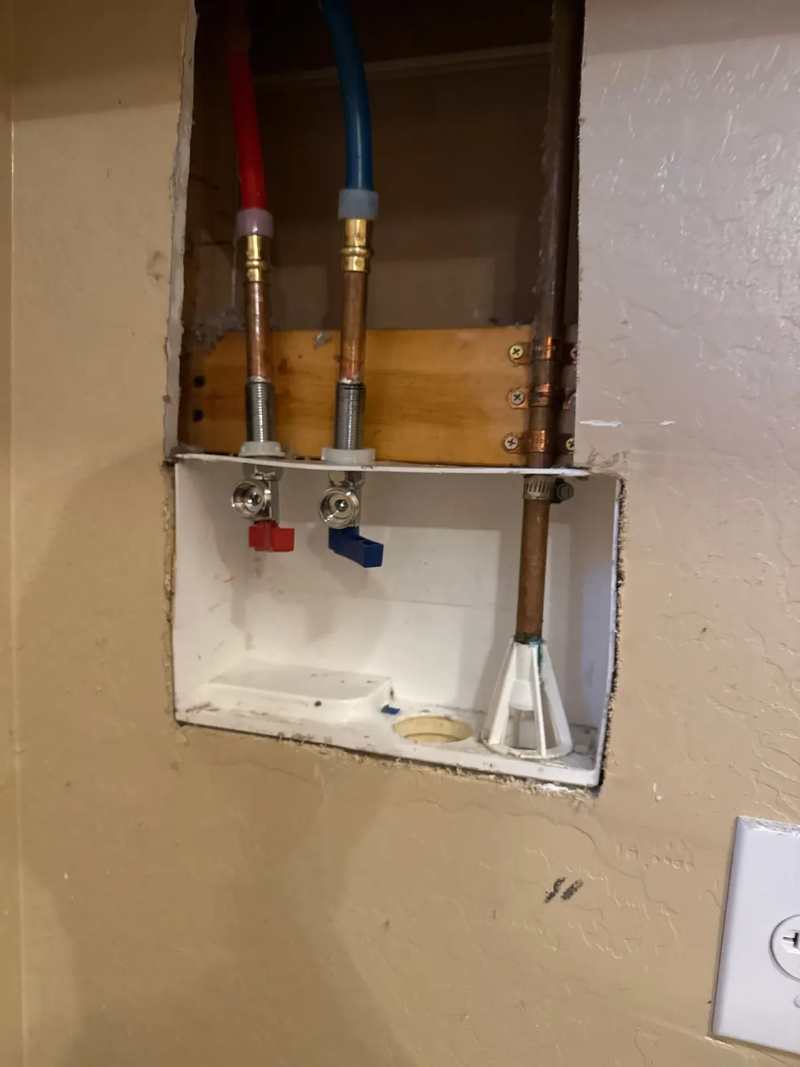 An opened laundry box wall showing the hot and cold supply lines and valves
