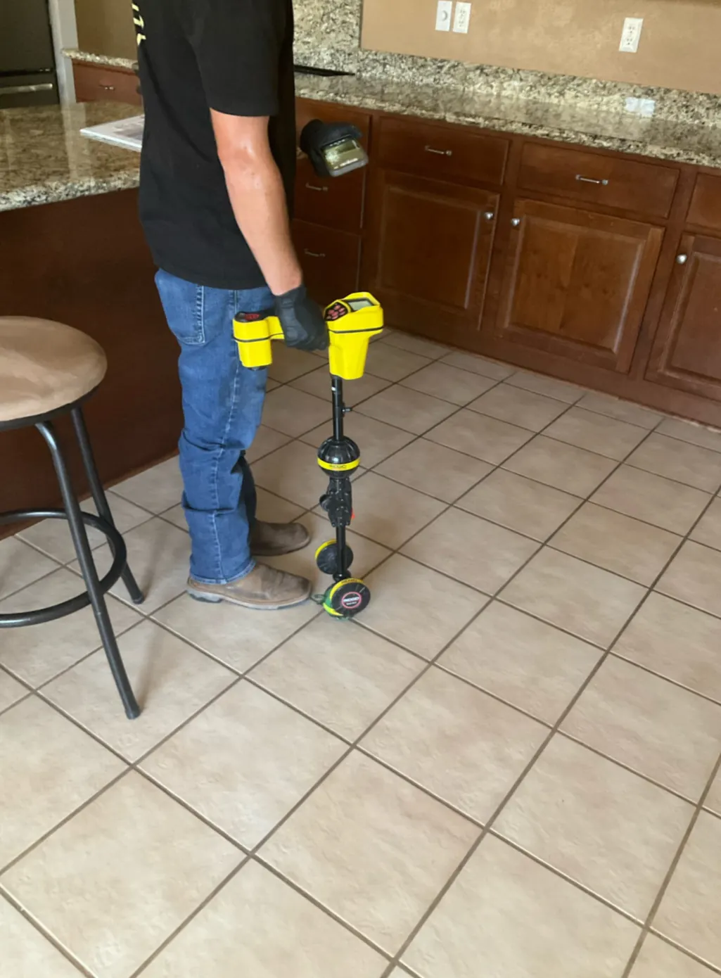 A technician using electronic leak-detection equipment on a tile kitchen floor