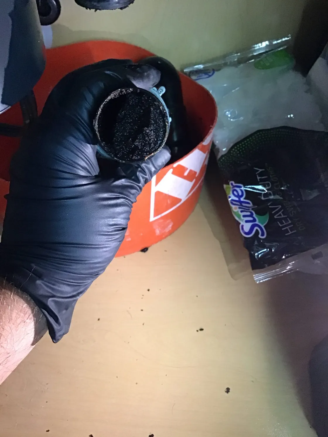 A gloved hand holding a drain fitting with material built up inside