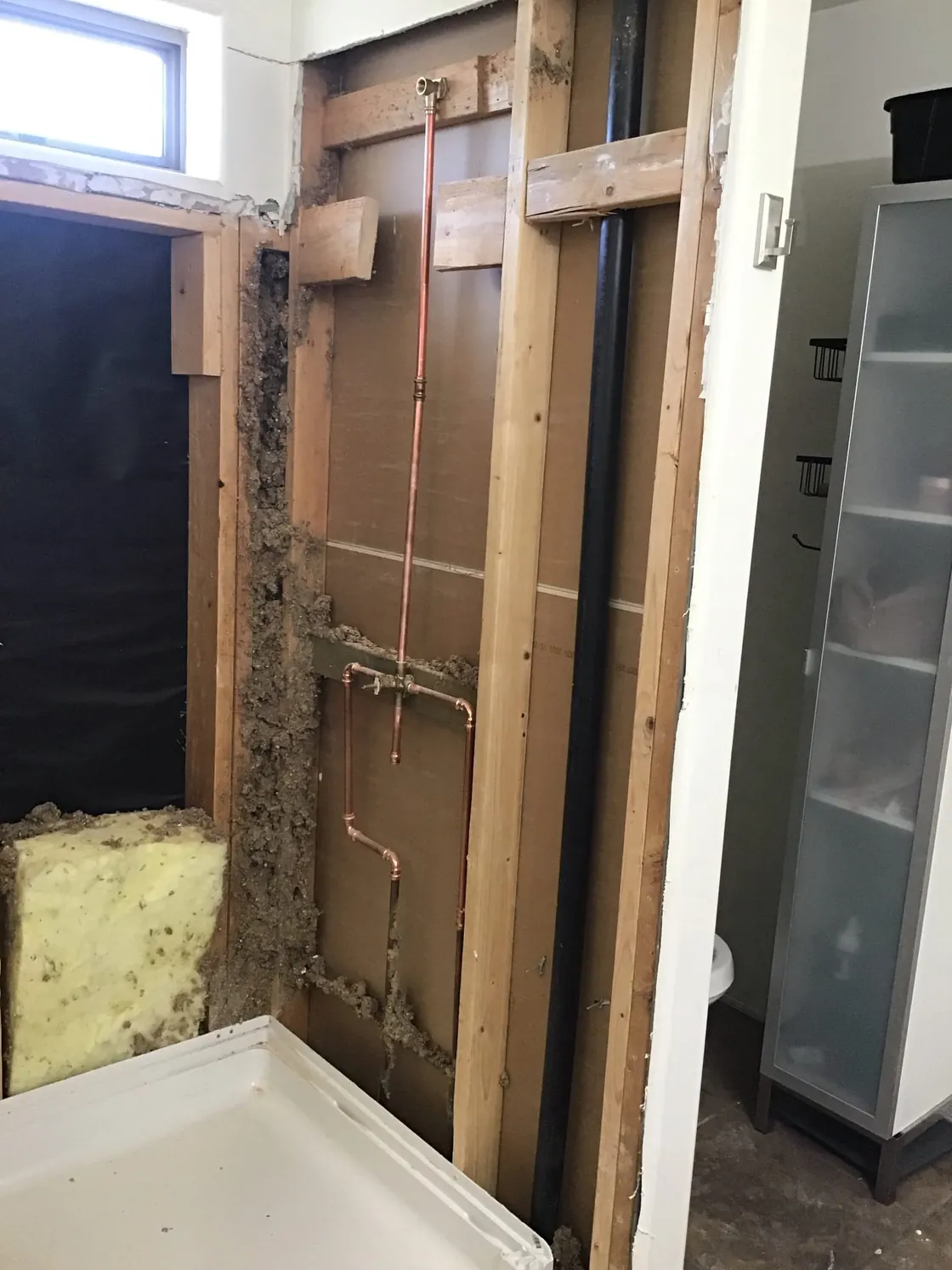 An opened shower wall with insulation pulled back and copper piping exposed
