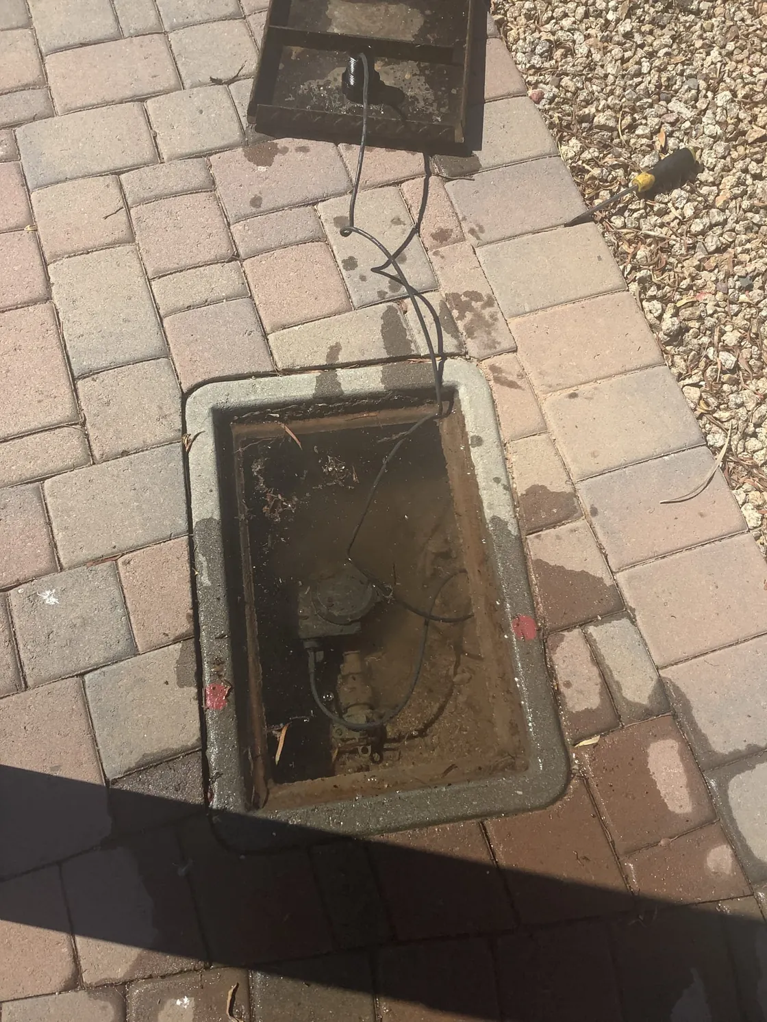 An opened water-line access box beside a paved walkway