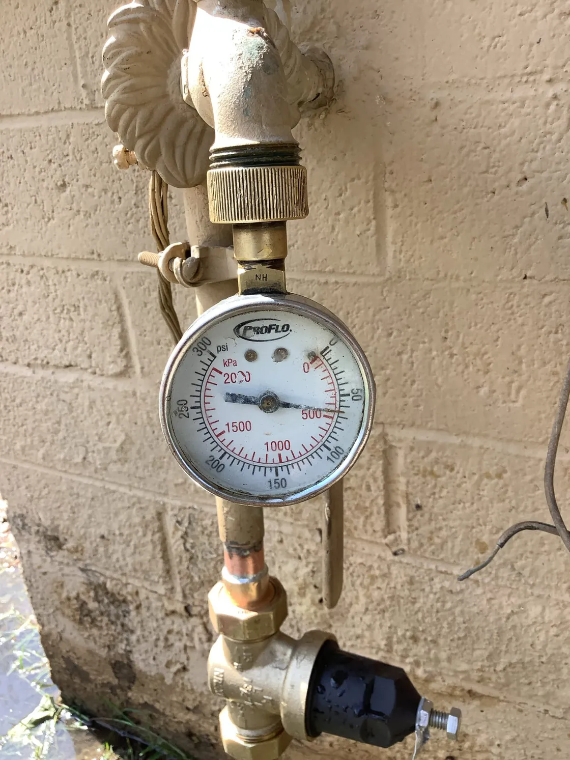A water pressure gauge attached to an outdoor faucet on a block wall