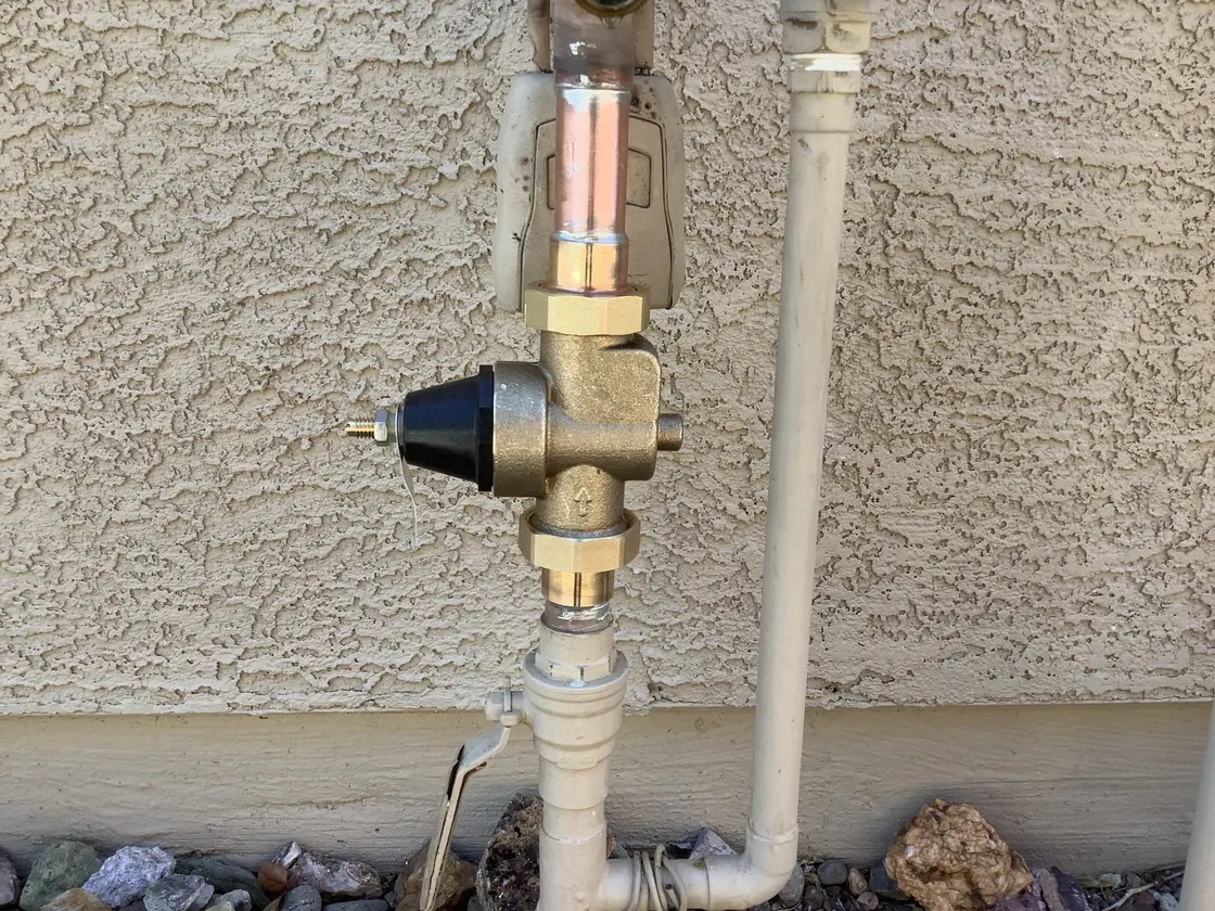 A brass pressure-reducing valve on a supply line against a textured stucco wall