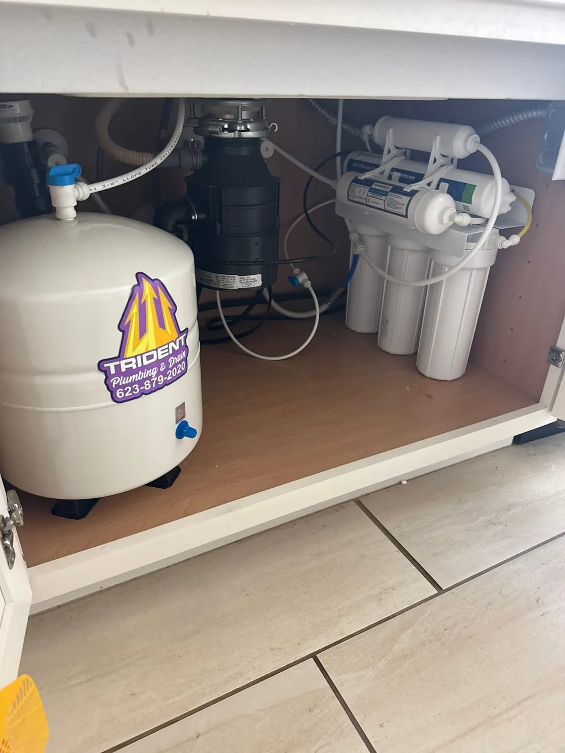 A reverse osmosis system and storage tank beside a garbage disposal in a sink cabinet