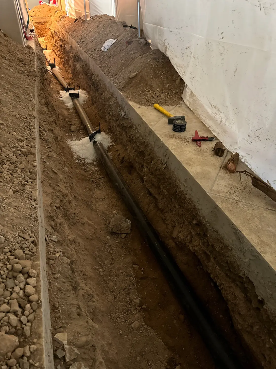 Replacement drain pipe in an open trench beside a building