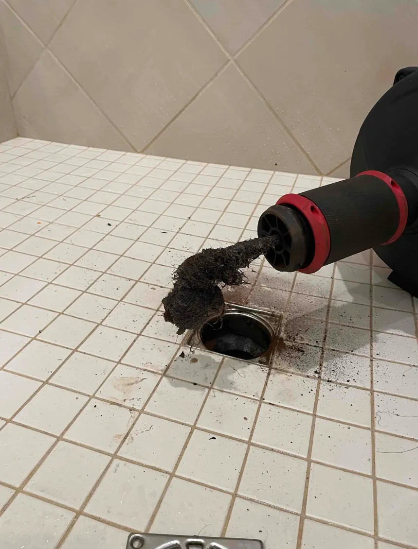A drain cable pulling a mass of hair and debris out of a tiled shower drain