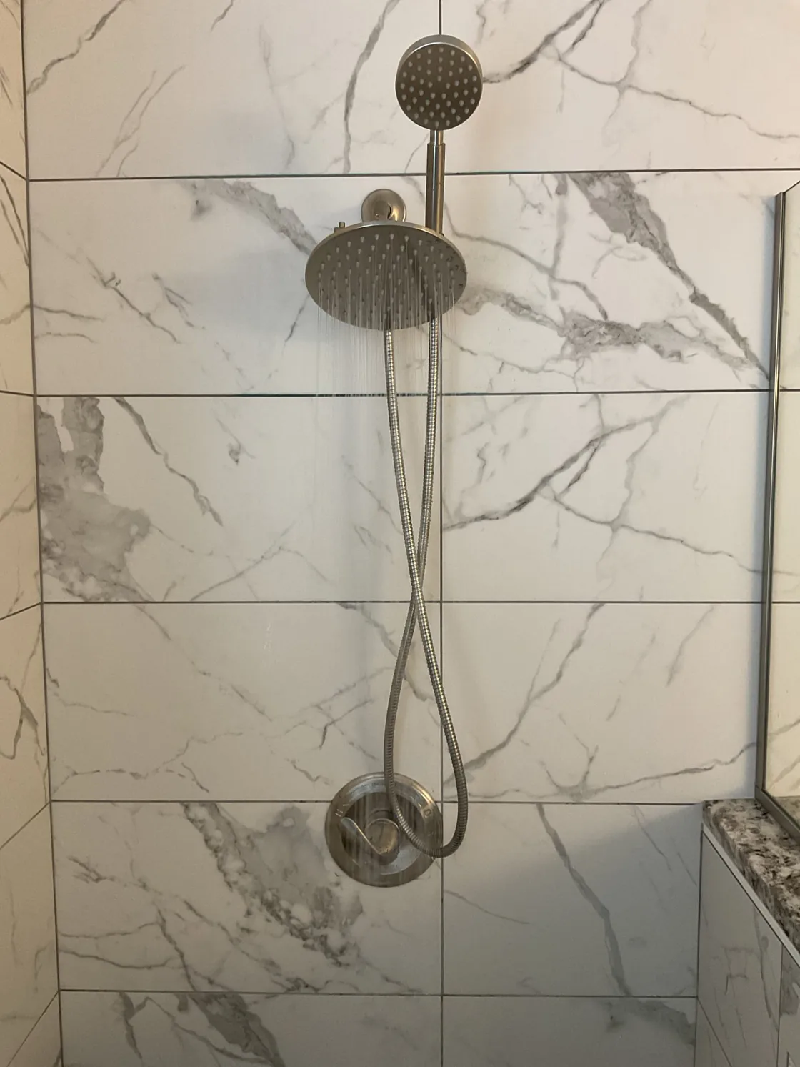 Two showerheads and finished shower trim on a marble wall