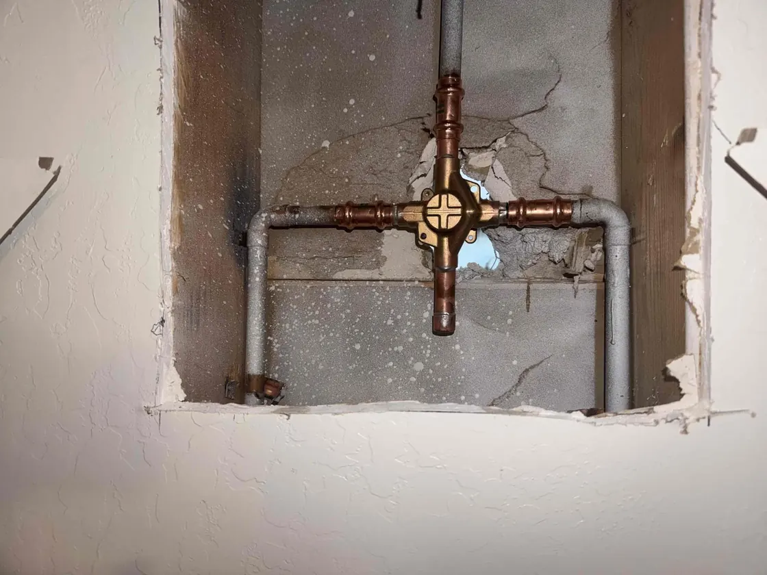 A shower valve and connected pipes visible through an opening in the wall