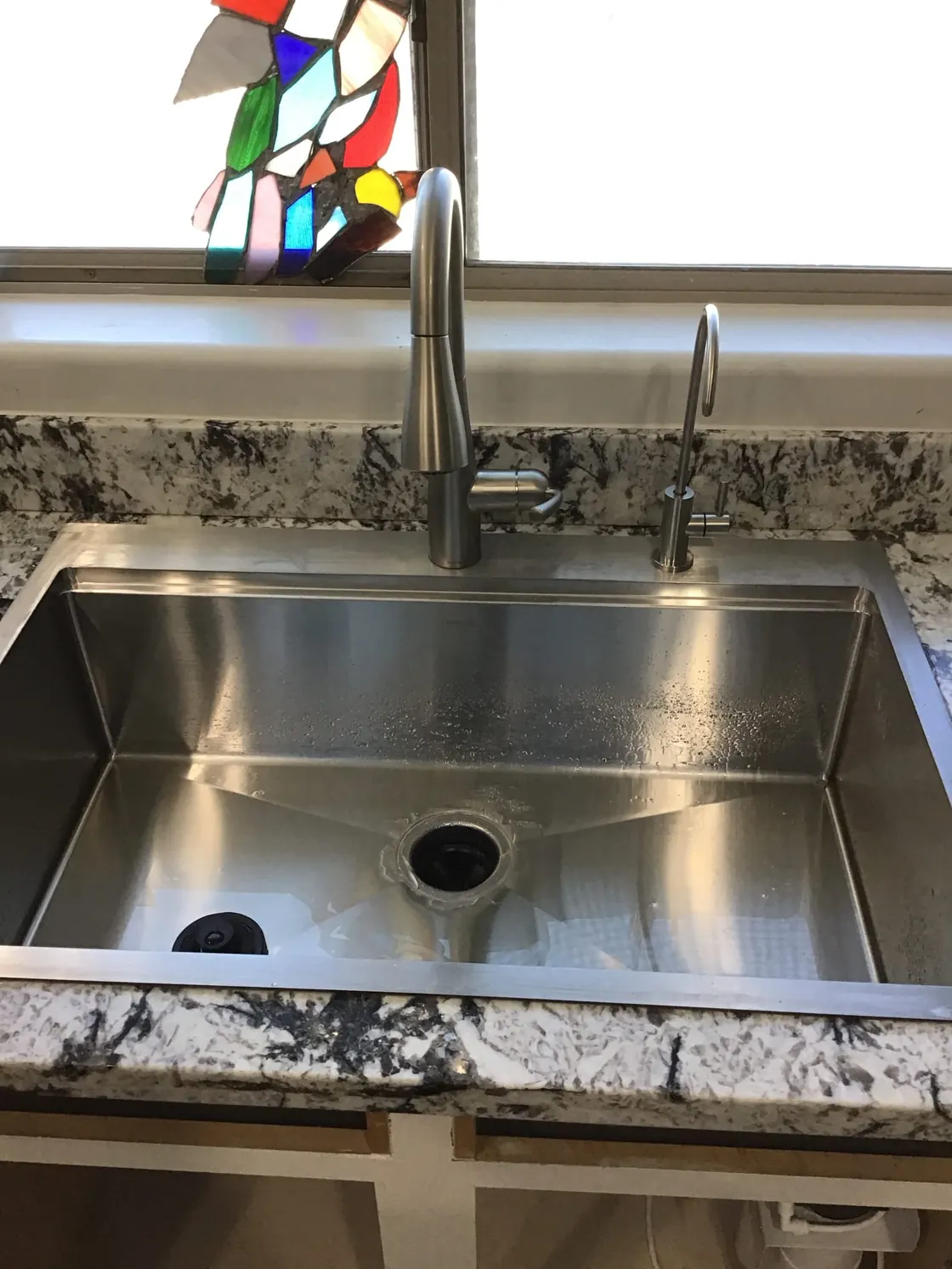 A stainless steel kitchen sink and tall faucet beneath a window