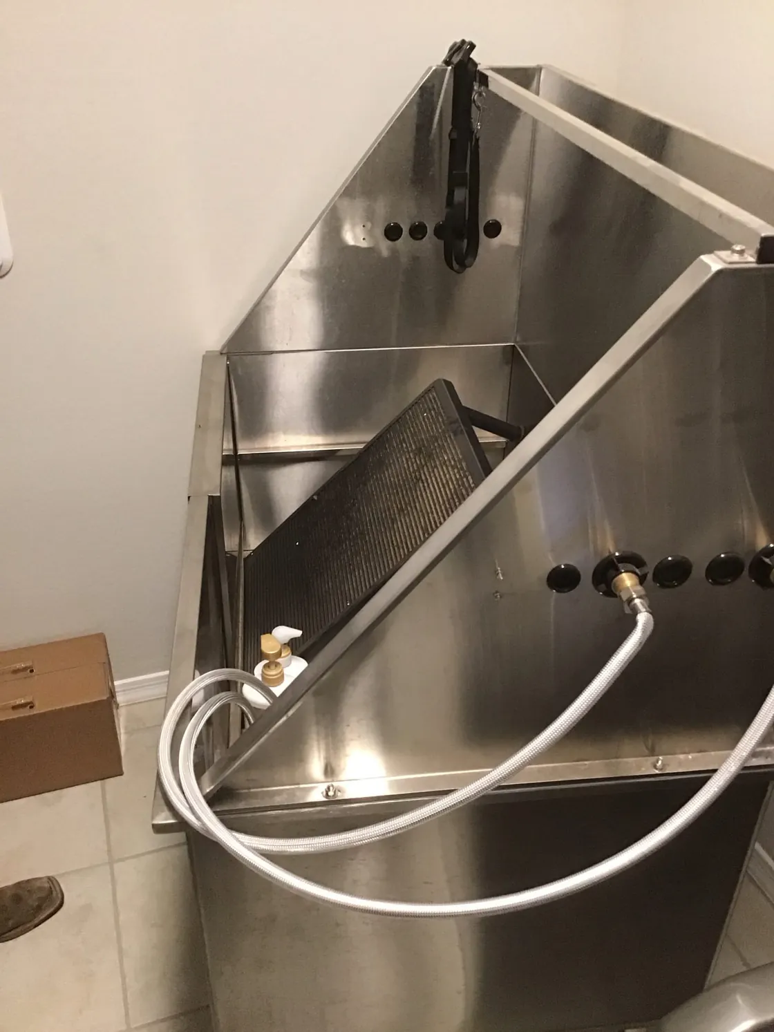 A large stainless steel utility sink with a sprayer hose and wall-mounted faucet