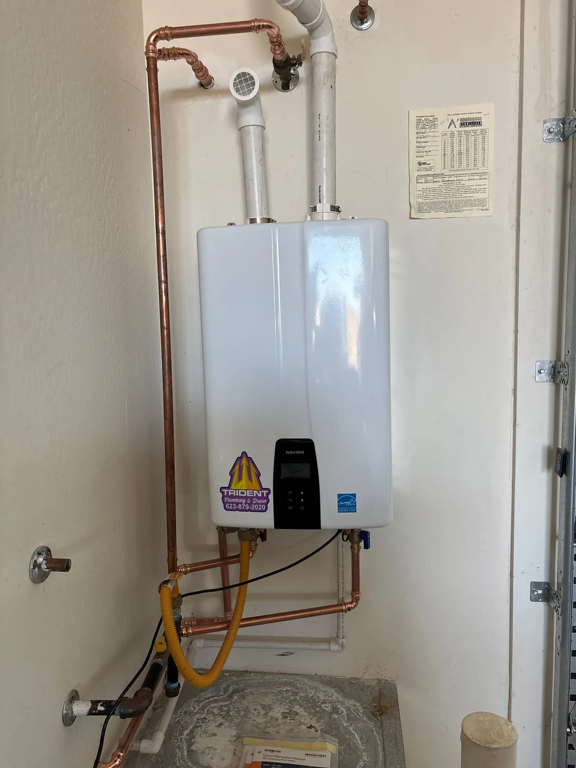 A tankless water heater in a closet with copper water lines and a yellow gas connector