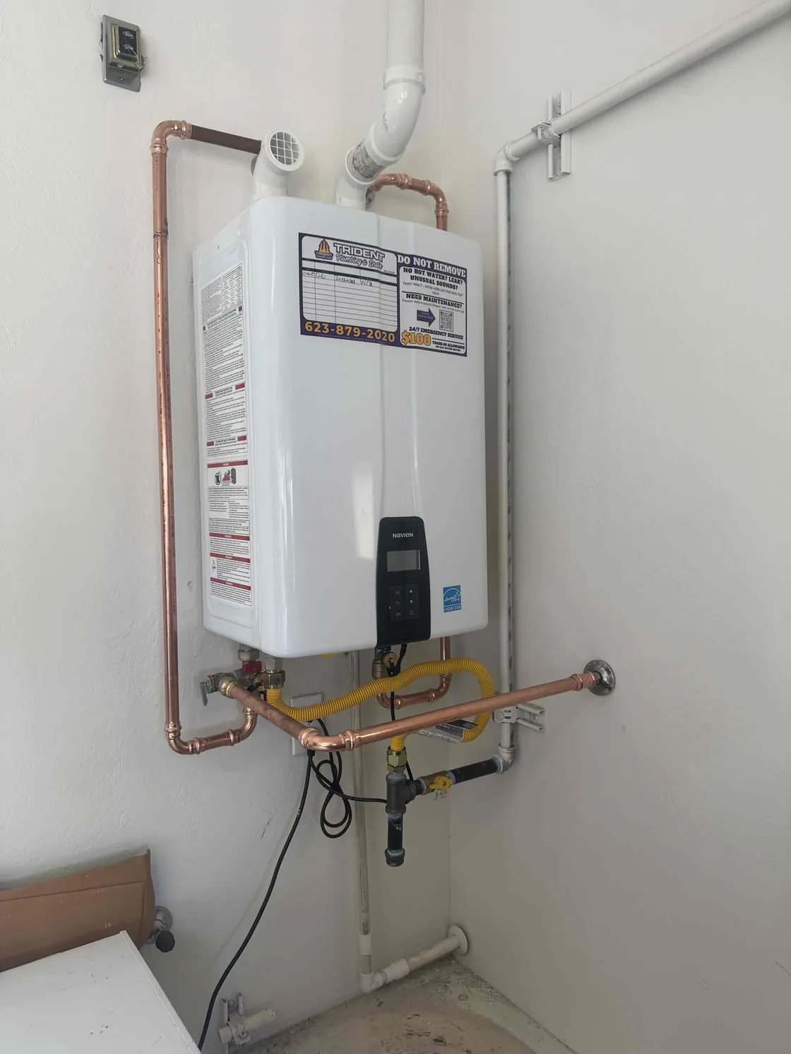 A tankless water heater mounted in a corner with copper water lines and venting